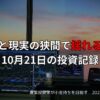 複数のモニターに株価チャートが映し出されたトレーディング環境。窓の外には夕焼けが広がり、画面上には「期待と現実の狭間で揺れる相場｜10月21日の投資記録」という日本語テキストが表示されている。