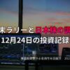 夕暮れの窓辺に並ぶ複数のモニターに株価チャートが表示されたトレーディングデスクの様子。年末ラリーと日本株の調整をテーマにした投資記録のイメージ。